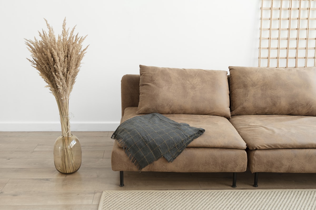 Charcoal wool throw draped over a tan sofa beside a vase of dried grass