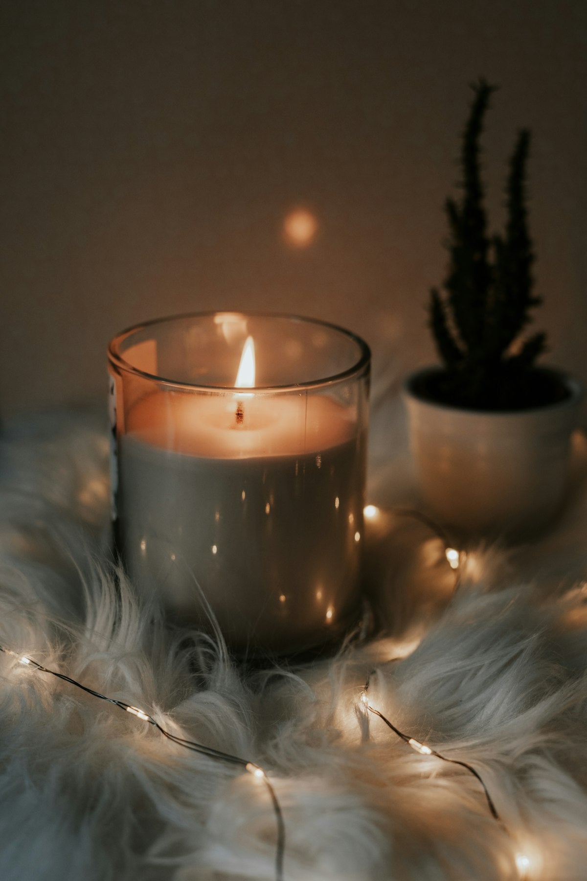 Lit Cedar & Amber soy candle in a glass jar on a sheepskin throw