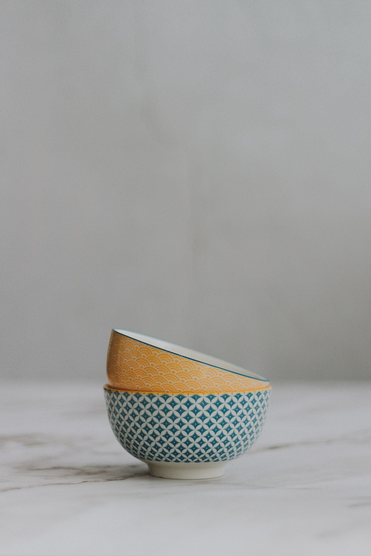 Stacked patterned breakfast bowls in ochre and teal on marble