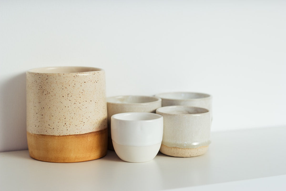 Speckled stoneware tumblers and crock on a white shelf